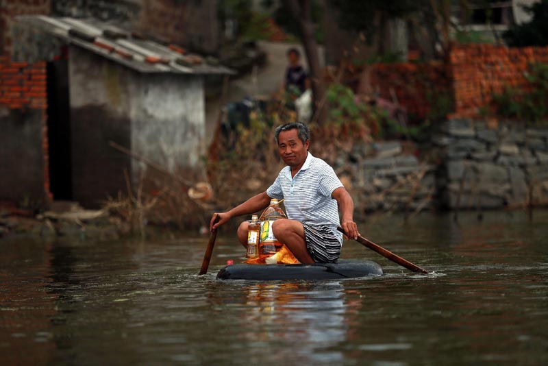 TWT06. Wuhan (China), 18/07/2016.- A picture made available on 23 July 2016 of a man paddling in a makeshift boat on flood water, Xinhua Village of Xinchang county in Wuhan city, Hubei Province of central China on 18 July 2016. Floods caused by heavy rainfall in north and central have killed more than 70 people, leaving many missing and hundreds of thousands homeless according to local reports. (Inundaciones) EFE/EPA/MARK CHINA OUT