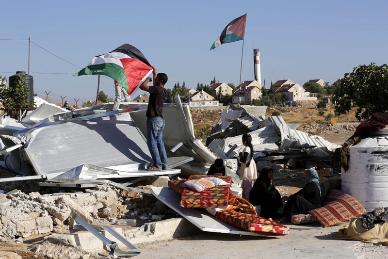 HEB17 HEBRÓN (PALESTINA) 09/08/2016.- Un joven palestino coloca una bandera palestina sobre su cobertizo derruido por tropas israelíes en la localidad cisjordana de Um Alkhair al sur de Hebrón hoy, 9 de agosto de 2016. Es la novena vez que la familia Hathaleen pierde sus cobertizos a manos de soldados israelíes en Um Alkhair, cerca del asentamiento de Karmael, ya que los palestinos no tienen los permisos israelíes para construir en la zona. EFE/Abed Al Hashlamoun