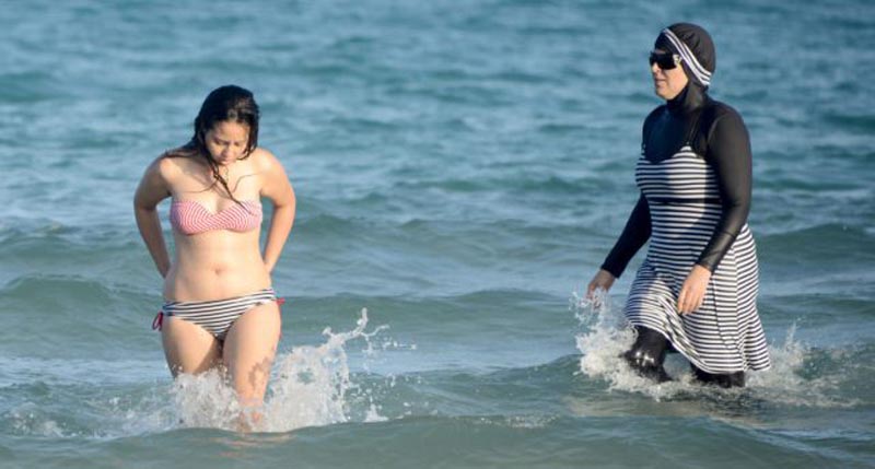 Tunisian women, one (R) wearing a "burkini", a full-body swimsuit designed for Muslim women, swim on August 16, 2016 at Ghar El Melh beach near Bizerte, north-east of the capital Tunis. / AFP / FETHI BELAID (Photo credit should read FETHI BELAID/AFP/Getty Images)