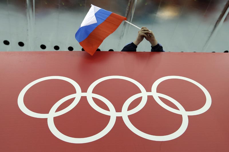 En imagen de archivo del 18 de febrero de 2015, un aficionado ruso al patinaje ondea la bandera de su país sobre los anillos olímpicos antes del inicio de la competencia de 10.000 metros de patinaje de velocidad en la Arena de Patinaje Adler, durante los Juegos Olímpicos de Invierno de Sochi 2014. El Comité Olímpico Internacional decidió el domingo 24 de julio de 2016 que no excluirá a toda la delegación rusa de participar en los Juegos Olímpicos de Rio 2016 debido a una red de dopaje auspiciada por el gobierno. (AP Foto/David J. Phillip, archivo)